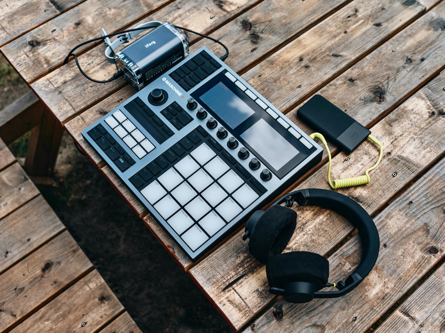 Top view of music production equipment including a controller and headphones on a wooden table.