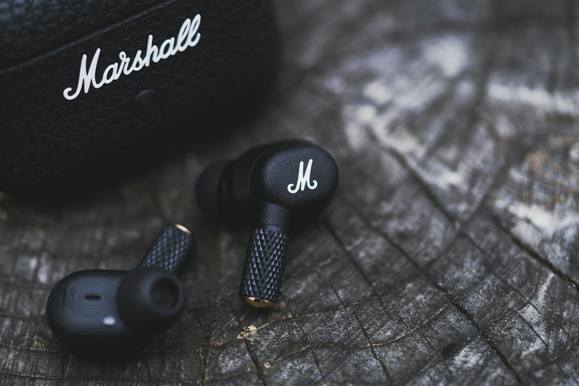 Close-up of black earbuds with textured design resting on a wooden surface, showcasing modern style.