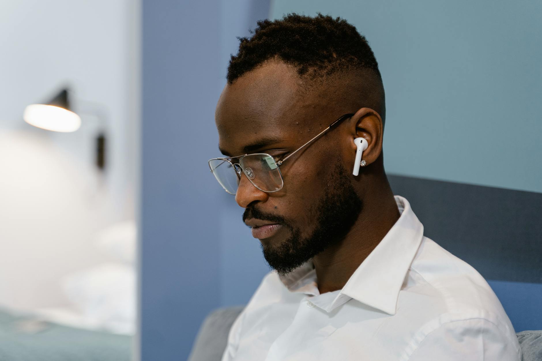 Man in glasses and earbuds working from home, concentrating on screen.