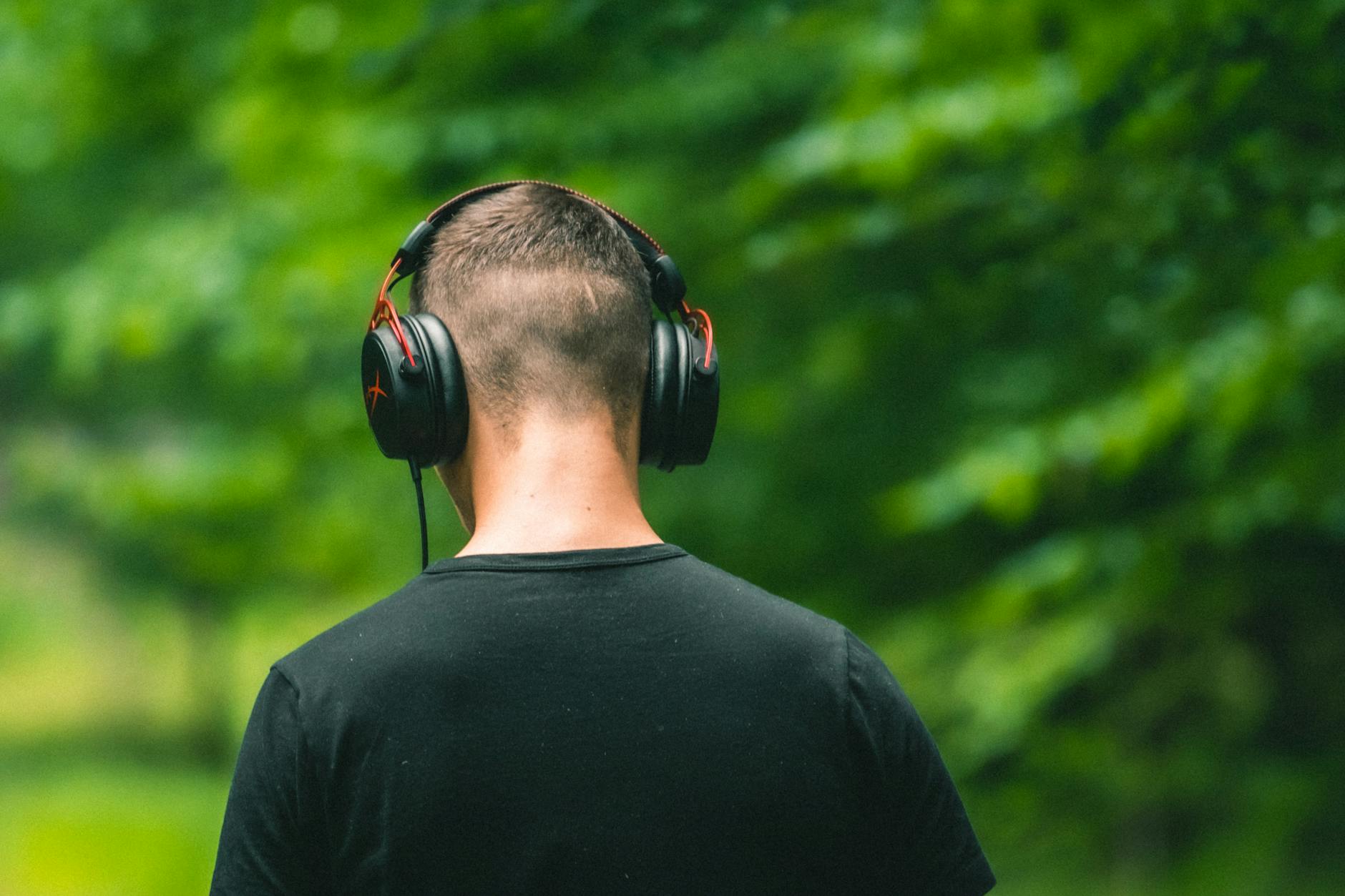 Adult man wearing headphones in a serene outdoor setting, surrounded by lush greenery.
