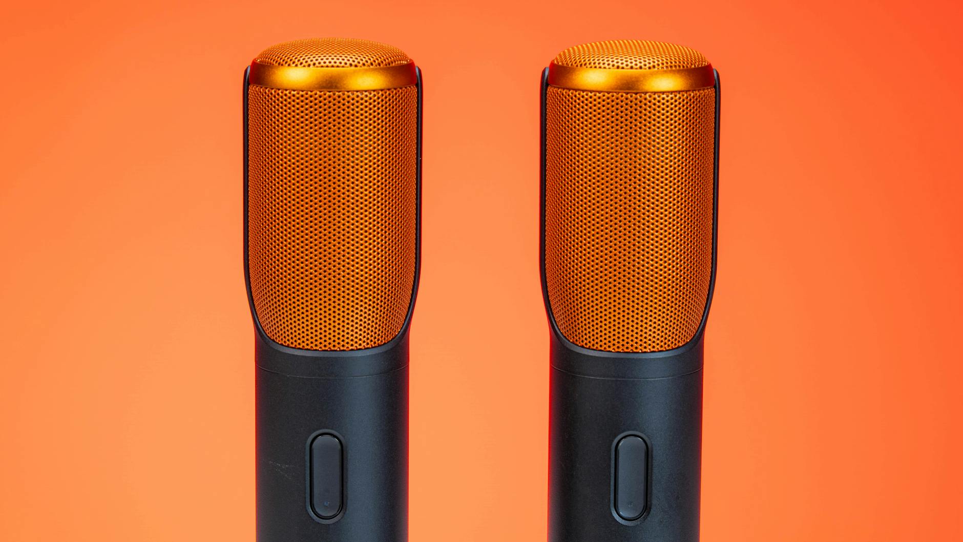 Vibrant photo of two modern microphones against an orange background, highlighting technology.